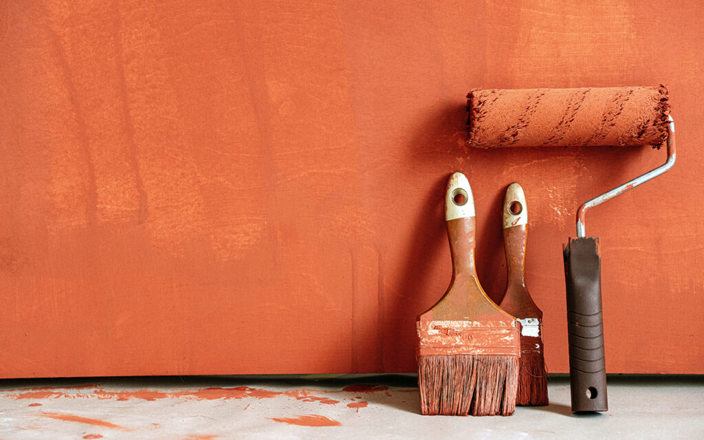 paint roller and brushes against an orange wall